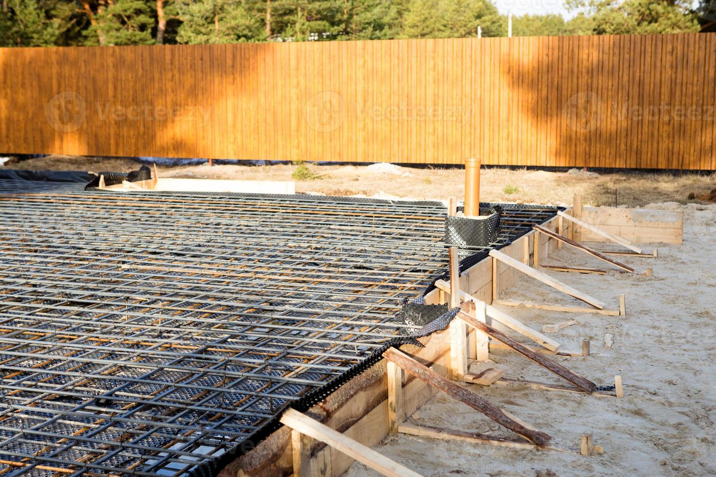 los accesorios de hierro en un encofrado de madera con tubos colocados son la base para verter los cimientos de la casa con una losa de hormigón. la construcción de las villas, el diseño, las comunicaciones de ingeniería. foto