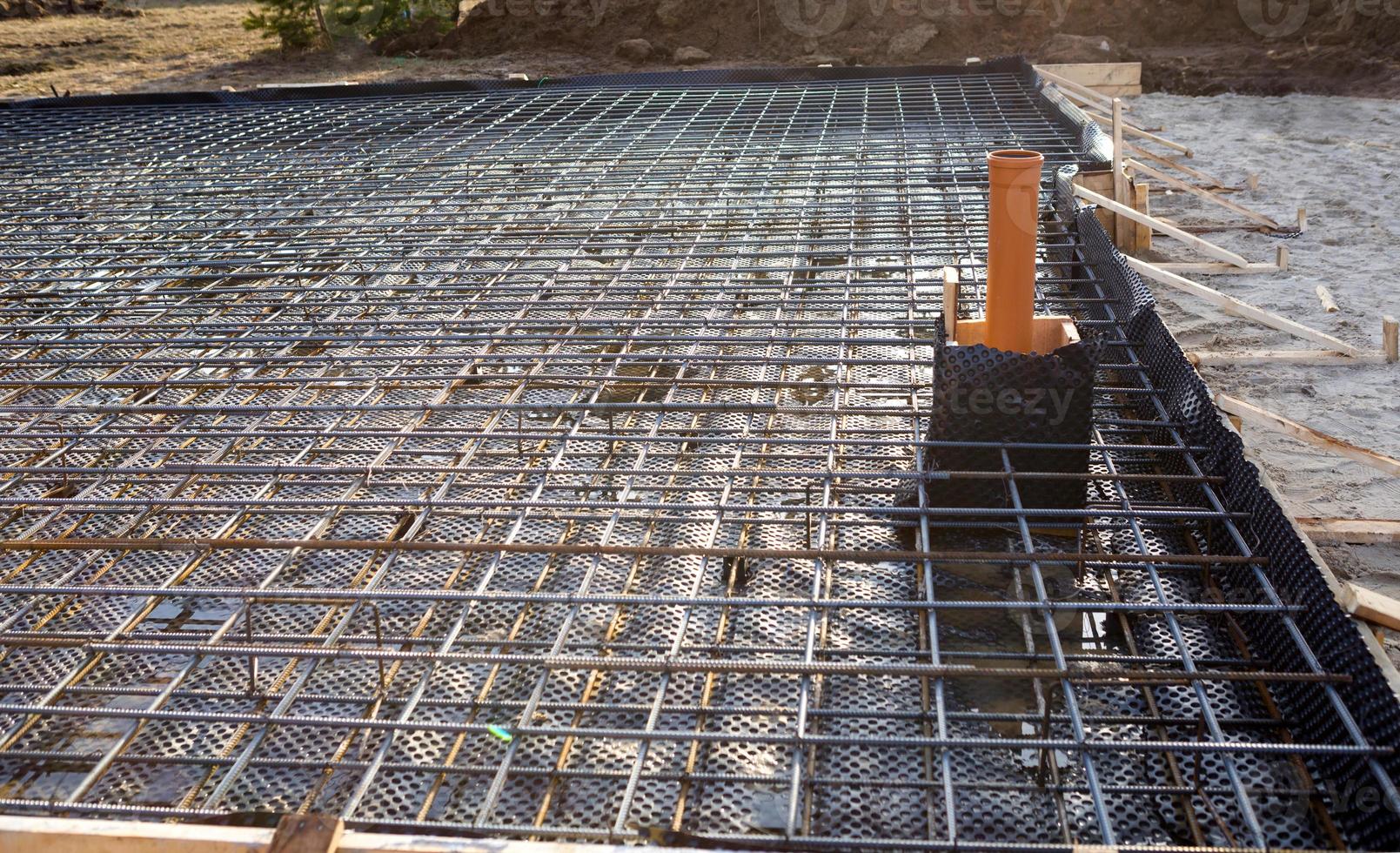 Iron fittings on a wooden formwork with laid pipes are the basis for pouring the foundation of the house with a concrete slab. Construction of cottages, design, engineering communications. photo