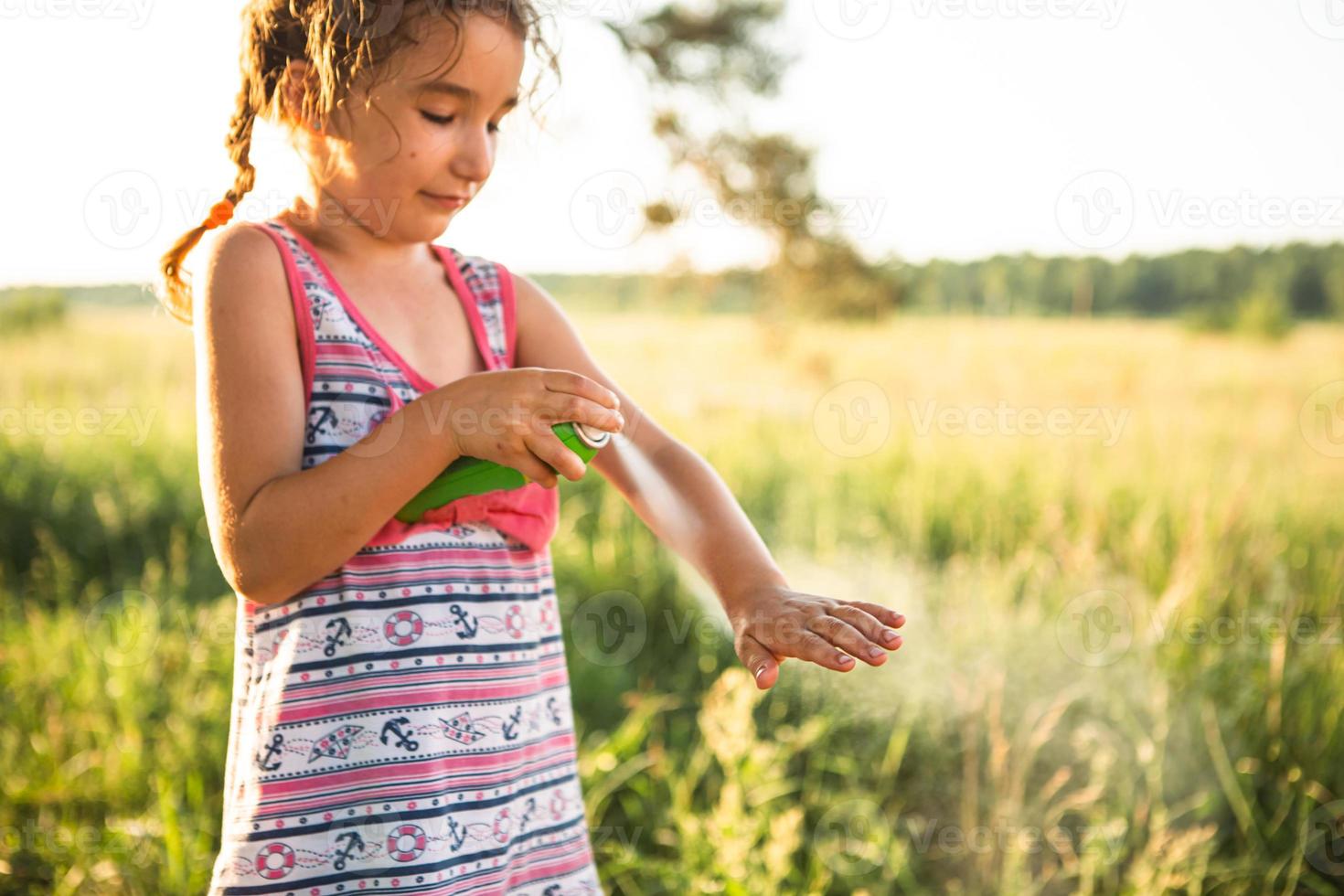 la chica rocía spray para mosquitos en la piel en la naturaleza que le muerde las manos y los pies. Protección contra picaduras de insectos, repelente seguro para niños. recreación al aire libre, contra las alergias. Hora de verano foto