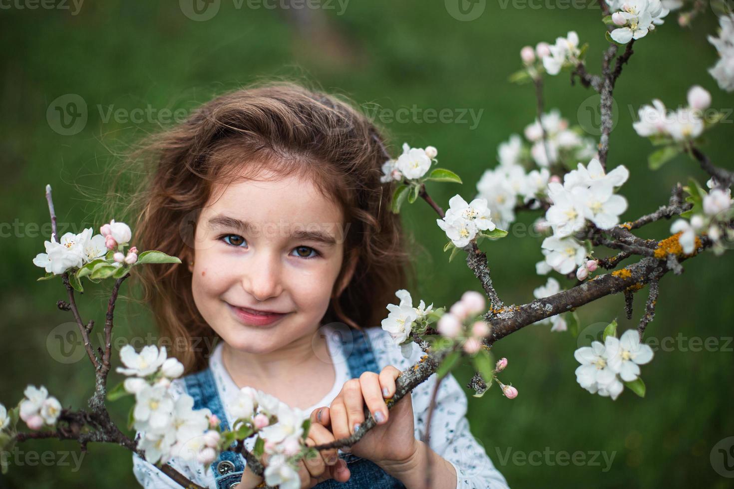 una linda niña de 5 años en un floreciente huerto de manzanas blancas en primavera. primavera, huerta, floración, alergia, fragancia primaveral, ternura, cuidado de la naturaleza. retrato foto