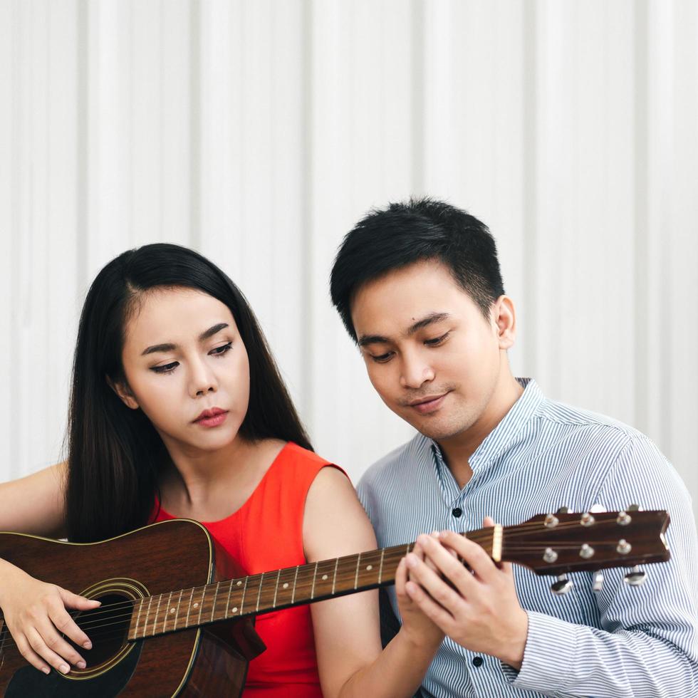 Man teaching how to play guitar to girlfriend at home on day photo