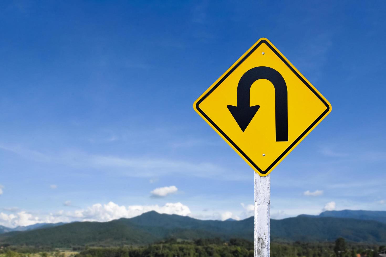 Left turn sign on white pole with clouds and blue sky background. photo