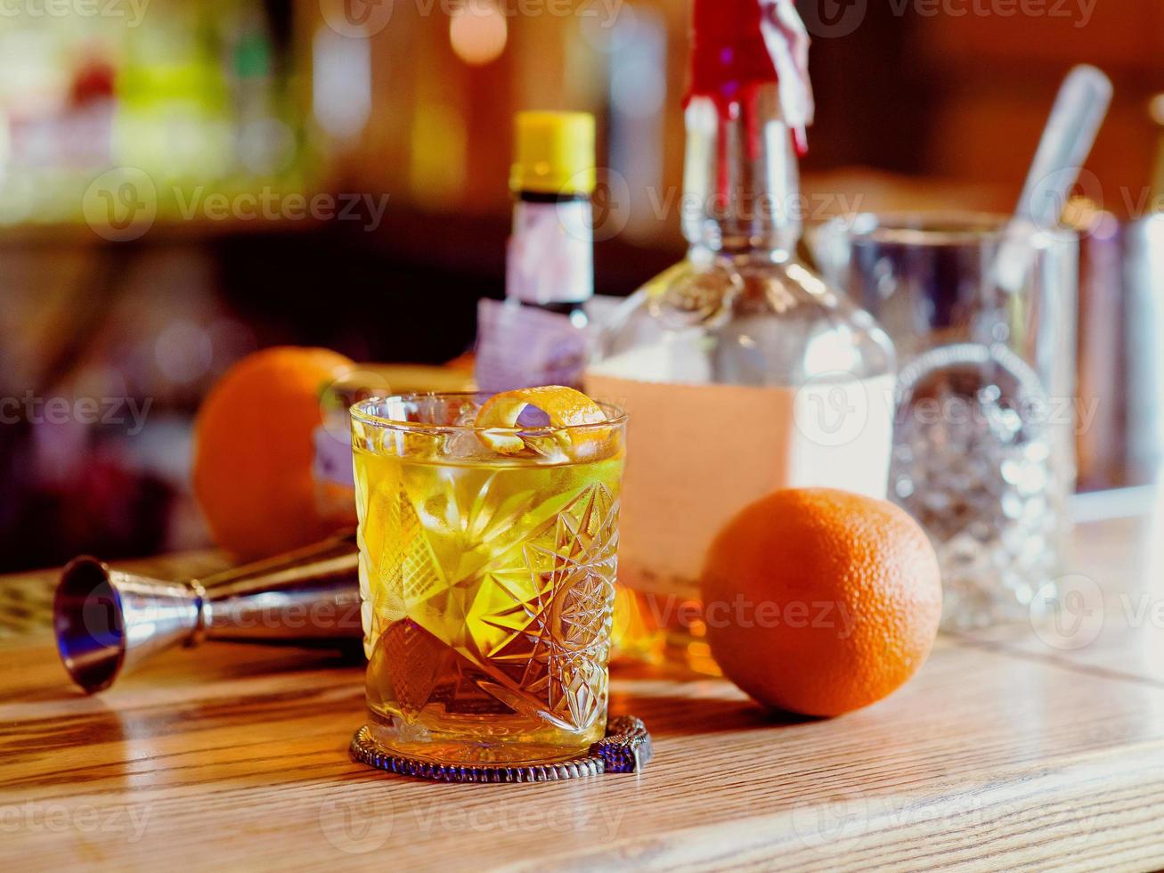 Old fashioned cocktail, orange, bottles and beaker on the bar counter photo