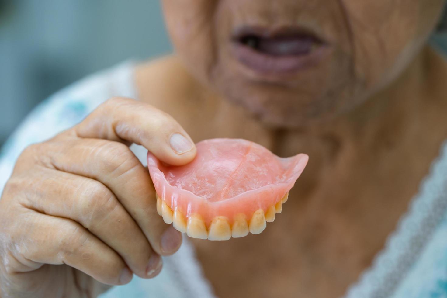 Asian senior or elderly old woman patient holding to use denture in nursing hospital ward, healthy strong medical concept photo