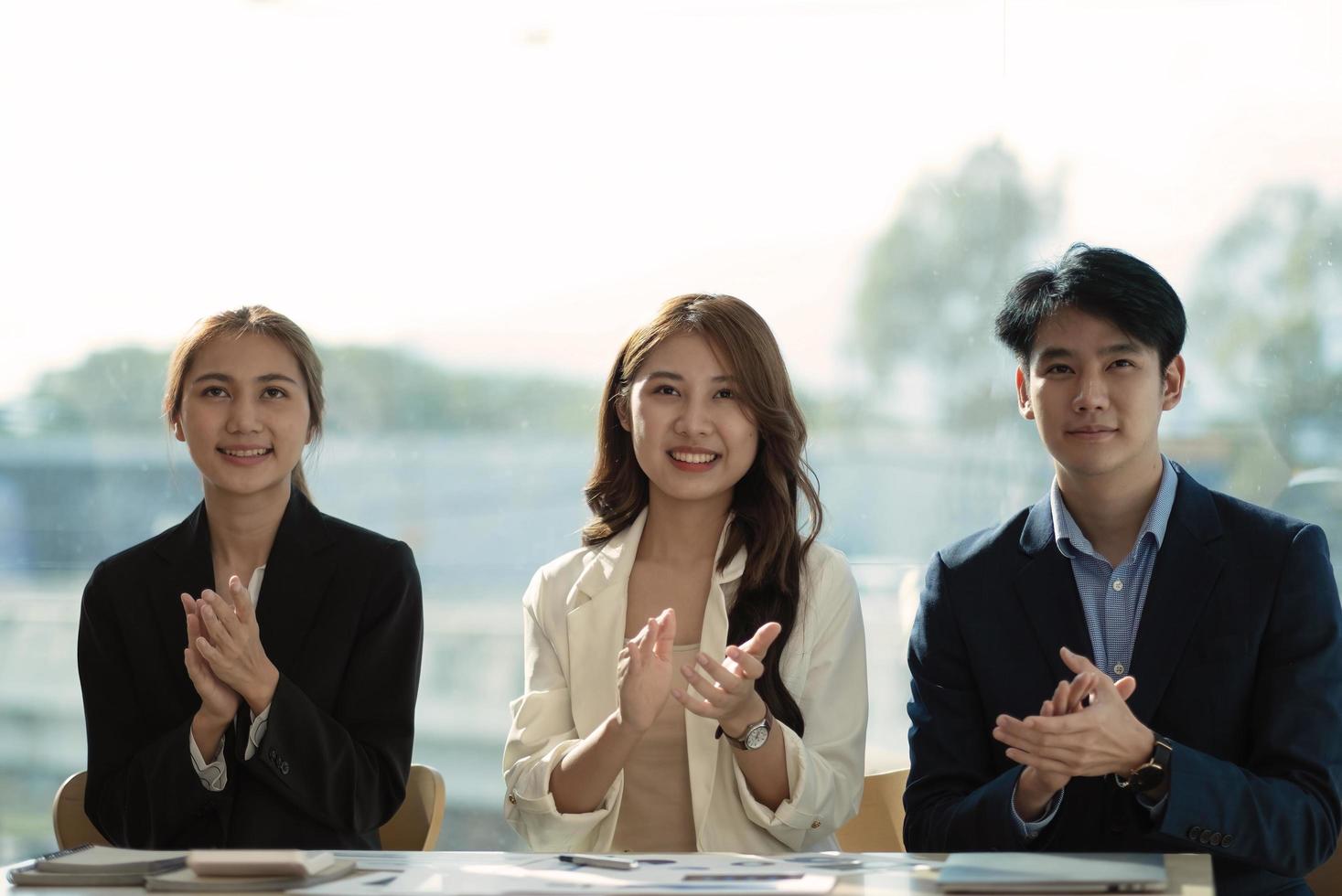 admire their success Front view of an Asian group of cheerful young people sitting in a meeting with applause. photo