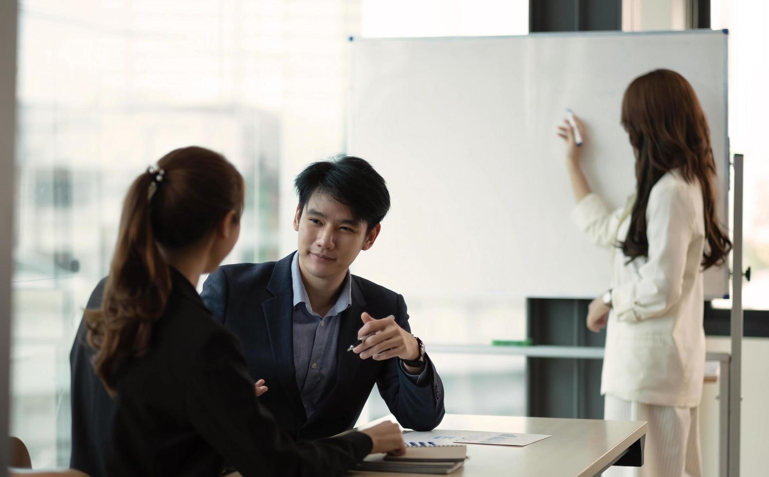 Confident businessman makes a presentation of a new project in the boardroom at a company meeting. Beautiful auditors talk with different partners about the business using a whiteboard and graphs. photo