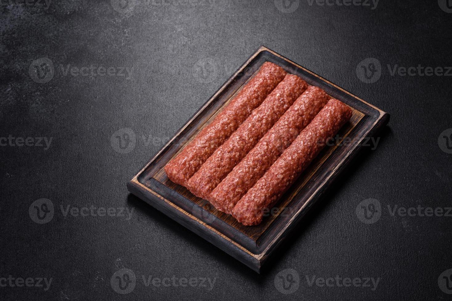 Fresh raw mince for grilled kebab with spices and herbs on a dark concrete background photo