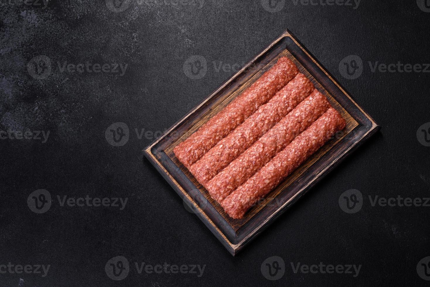 Fresh raw mince for grilled kebab with spices and herbs on a dark concrete background photo