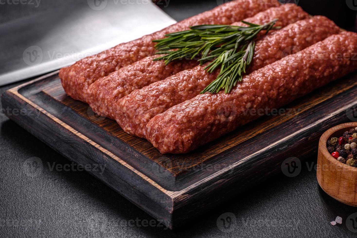 Fresh raw mince for grilled kebab with spices and herbs on a dark concrete background photo