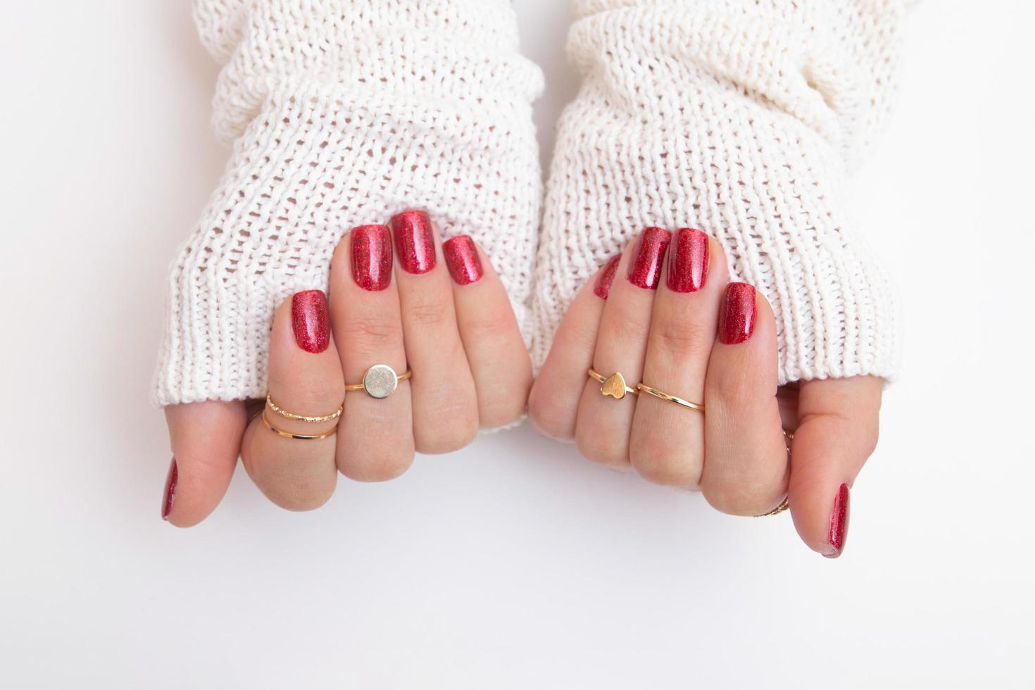 Gel polish for manicure of red color with sparkles on female hands with rings and a sweater photo