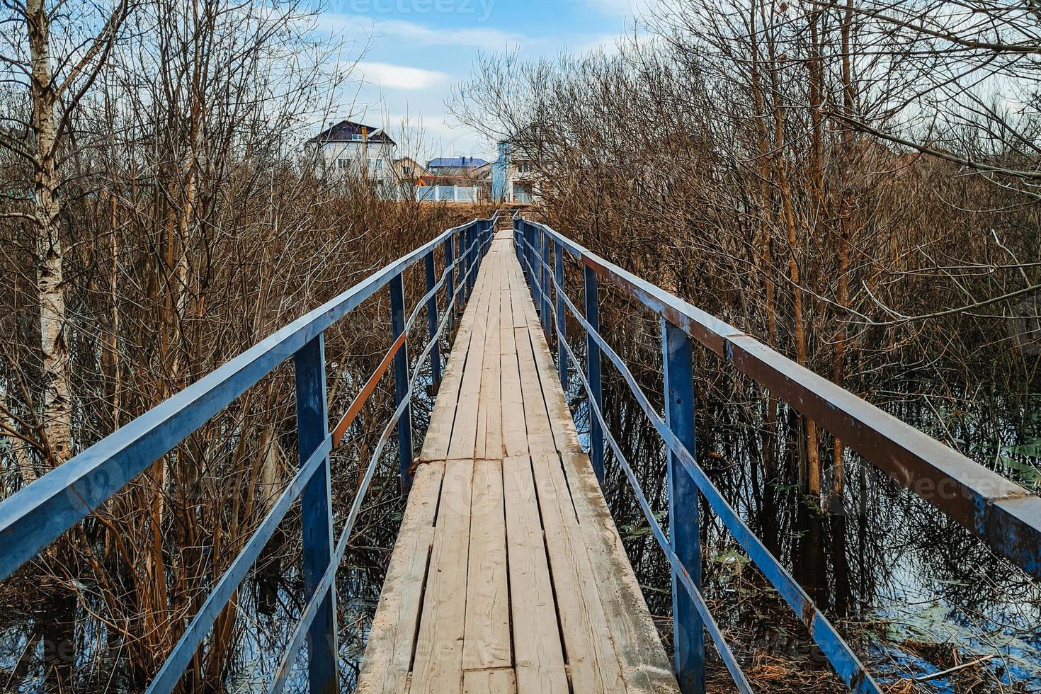 Old wooden bridge over the river in village. Narrow pedestrian crossing. photo