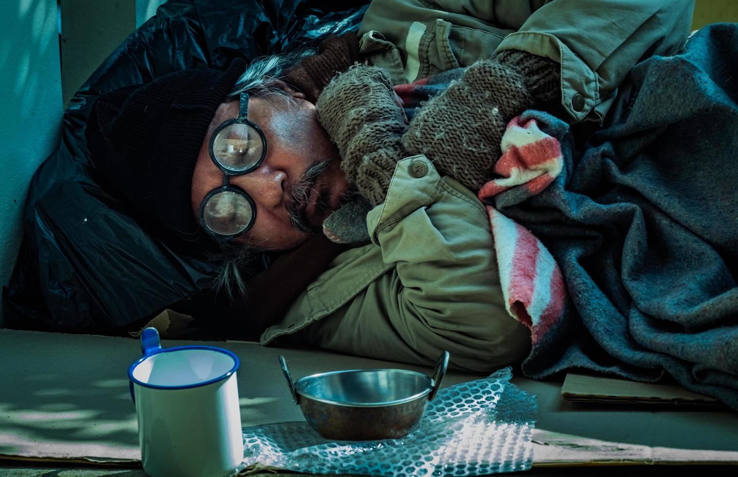 el hombre sin hogar duerme en el suelo con una taza y una olla para recibir ayuda y asistencia. foto