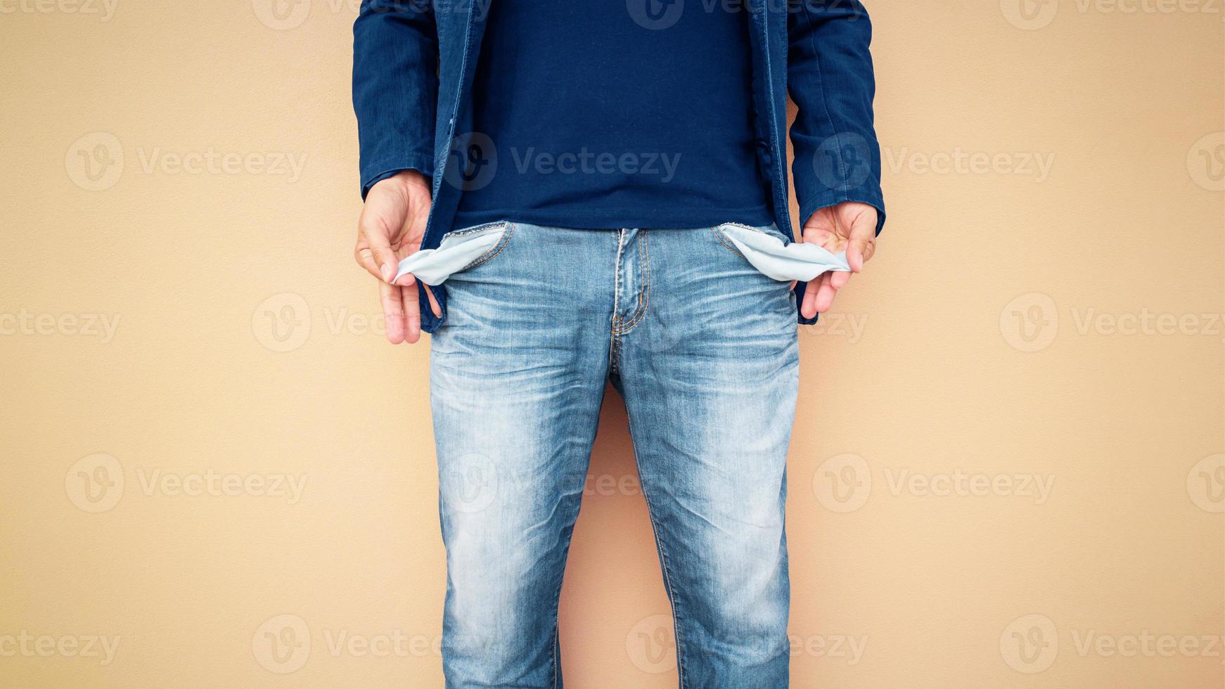 Man showing his empty pockets on cement wall background. photo