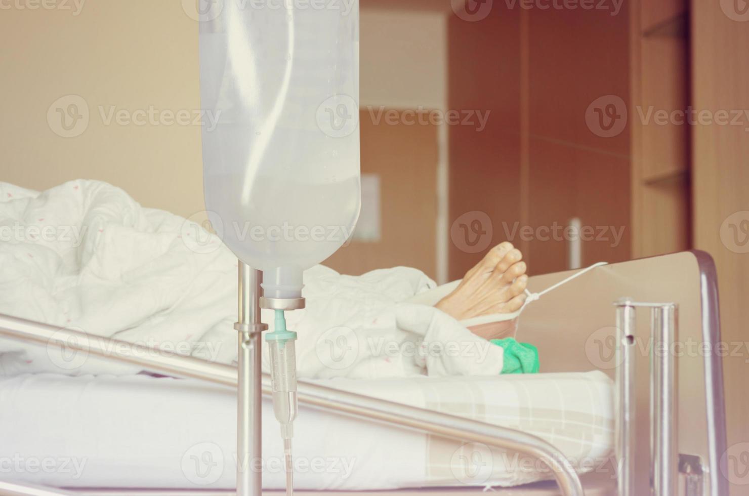 Asian elderly women patient's hand on a drip receiving a saline solution holding on to the bed in hospital photo