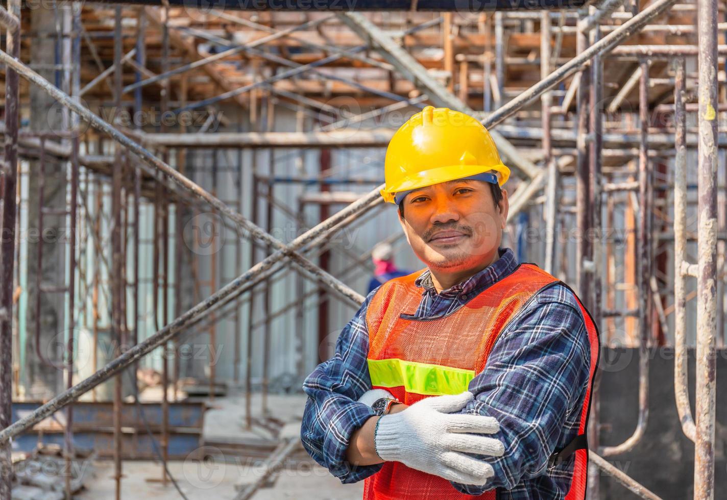 proyecto de control y planificación de trabajadores en el sitio de construcción, hombre sonriente con los brazos cruzados sobre fondo borroso foto