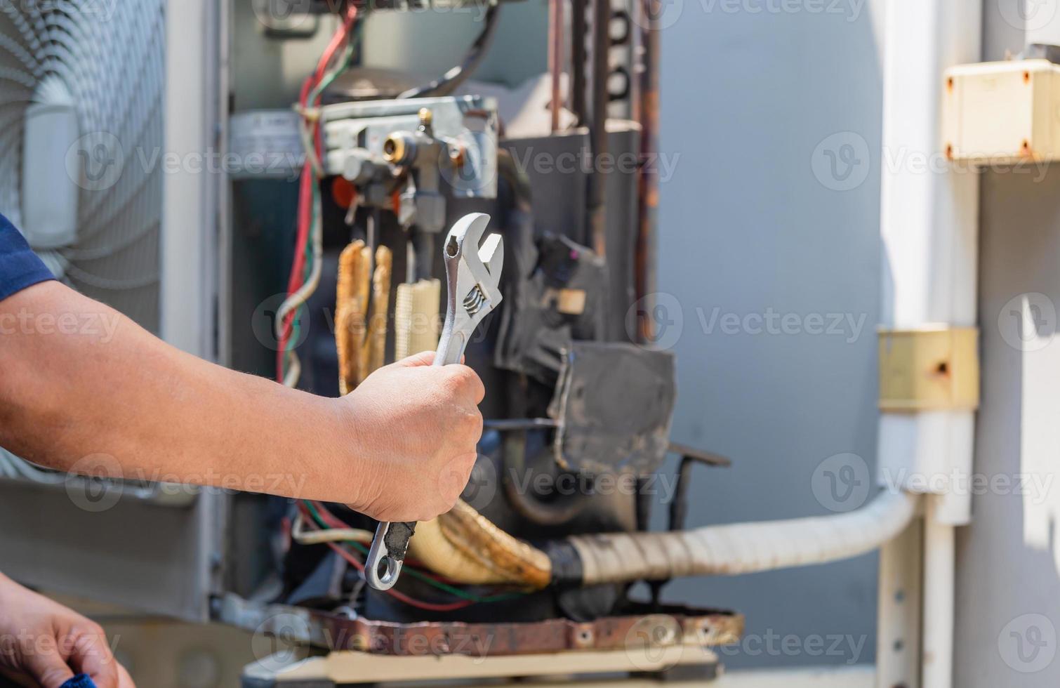 Selective focus of technician man hands holding a wrench over blurred modern air conditioning, Maintenance and repairing concept photo