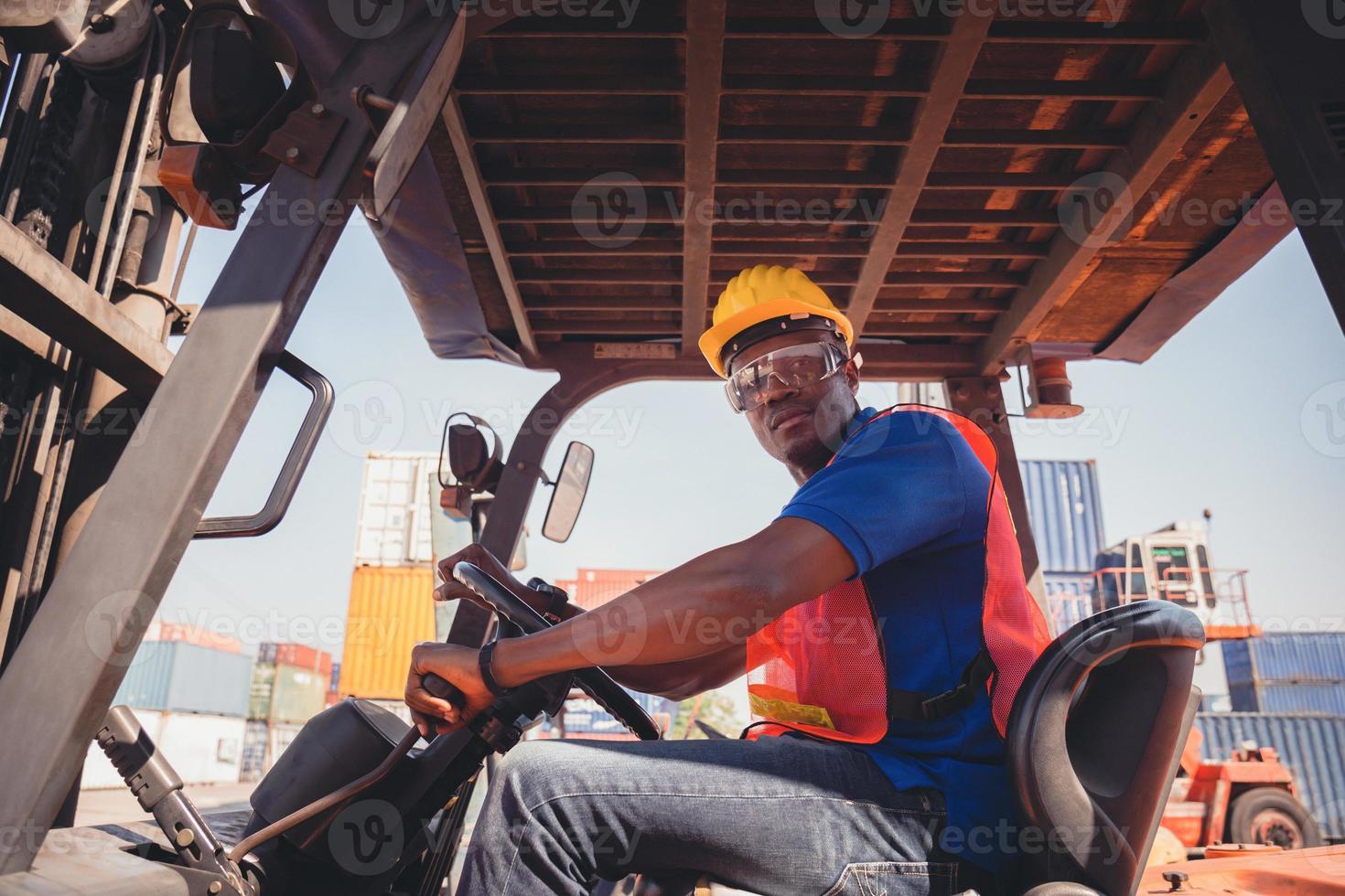 Worker man in hardhat and safety vest sitting in container stackers control loading containers box from cargo photo