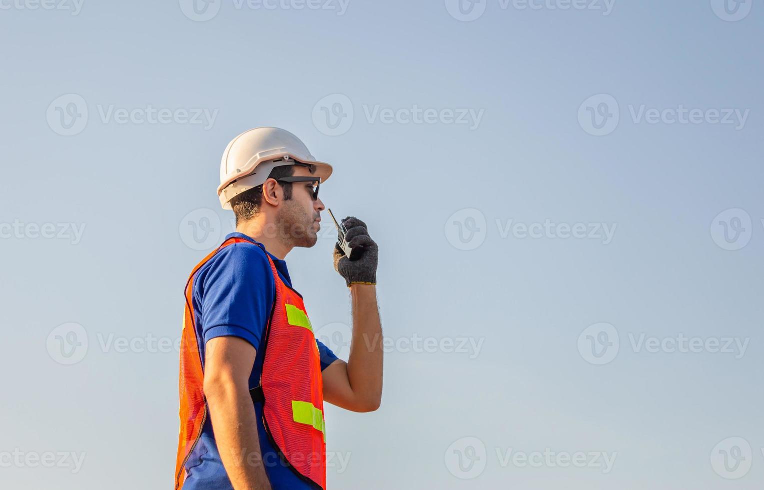 Foreman in hard hat and safety vest talks on two-way radio at containers cargo photo