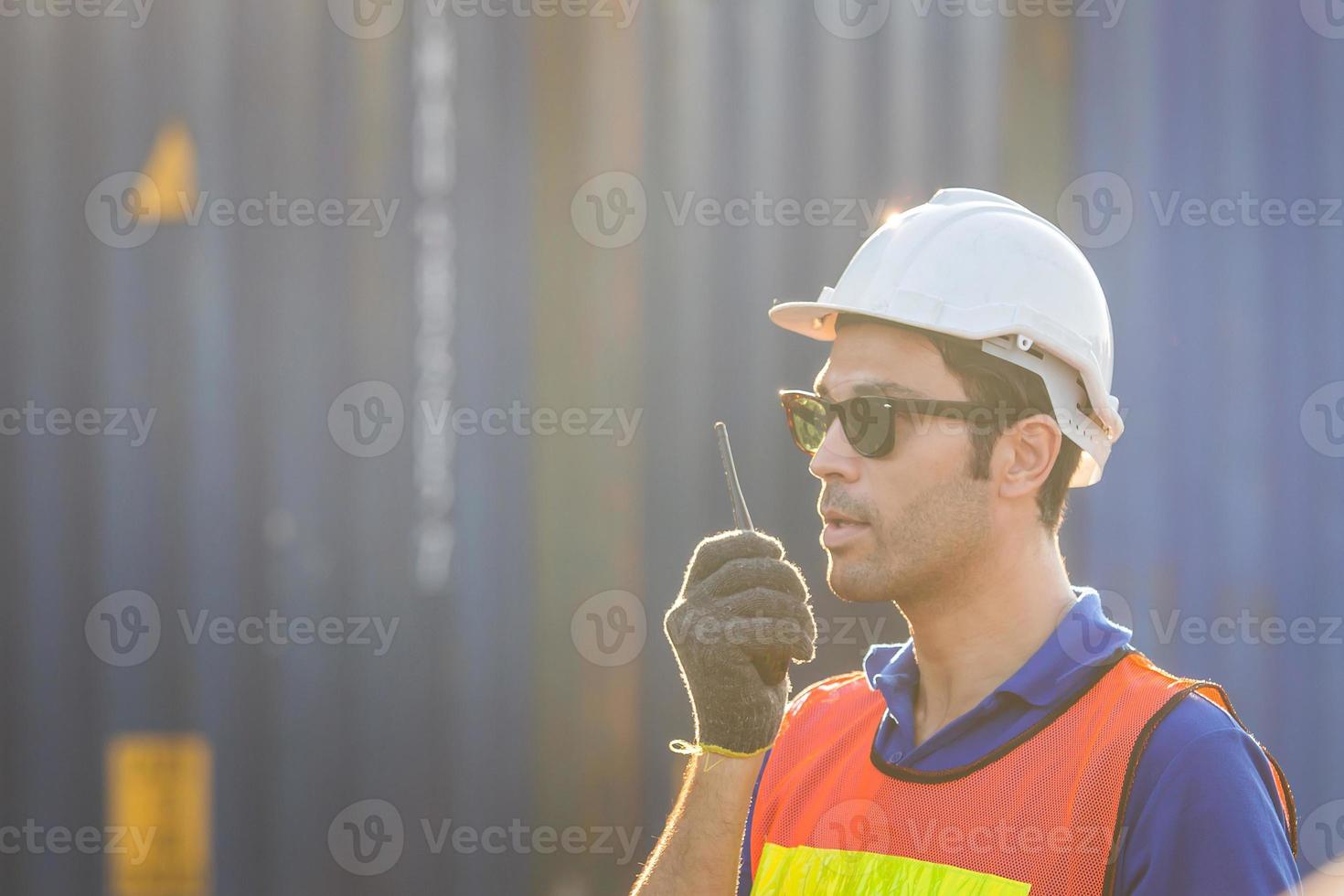 Foreman in hardhat and safety vest talks on two-way radio, Factory worker control loading containers box from cargo photo