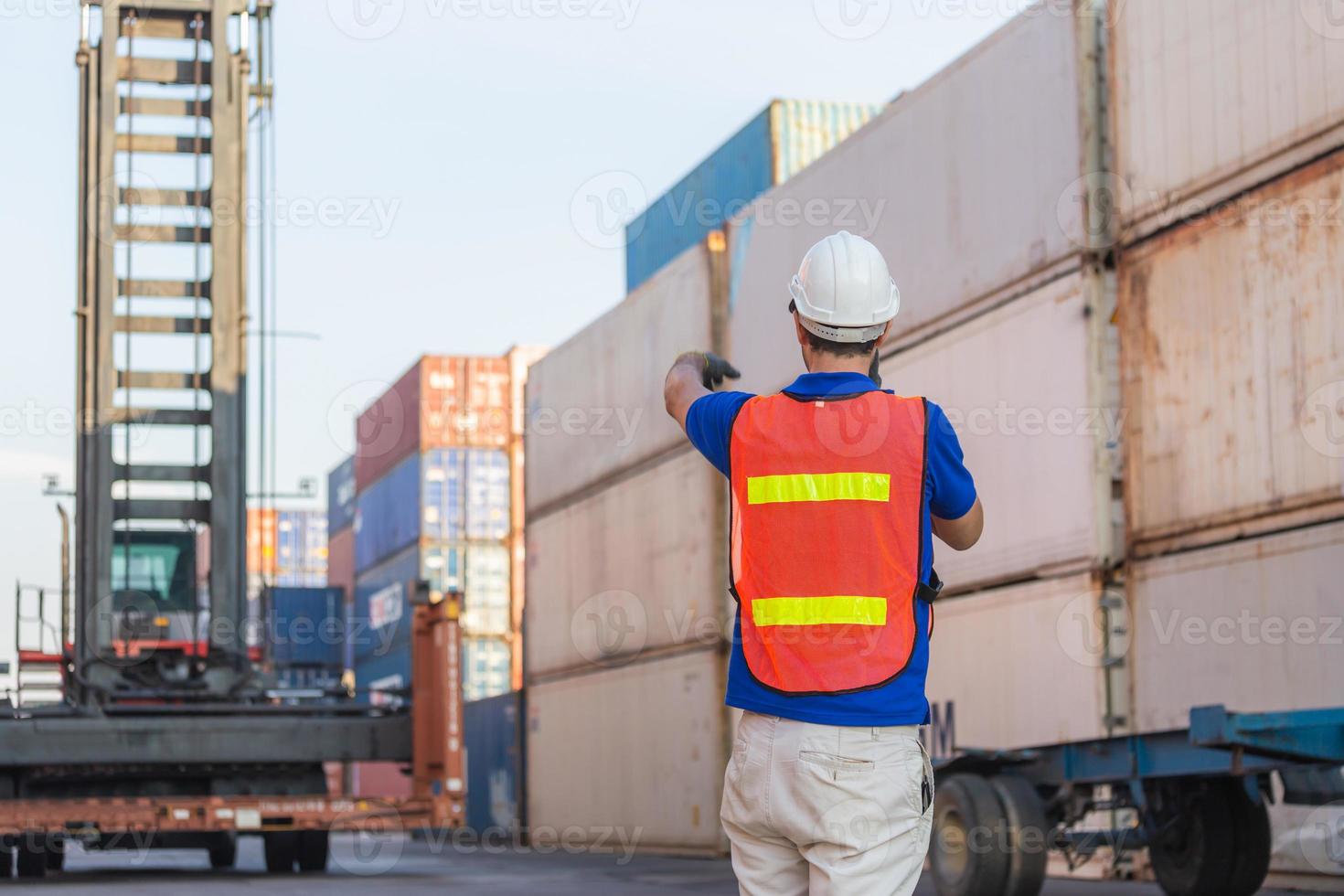 Foreman in hardhat and safety vest talks on two-way radio control loading containers box from cargo photo