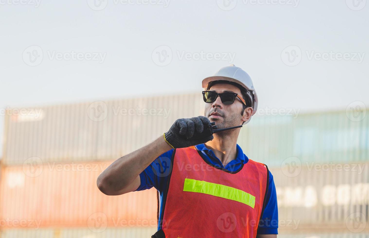 Happy foreman in hardhat and safety vest talks on two-way radio control loading containers box from cargo photo