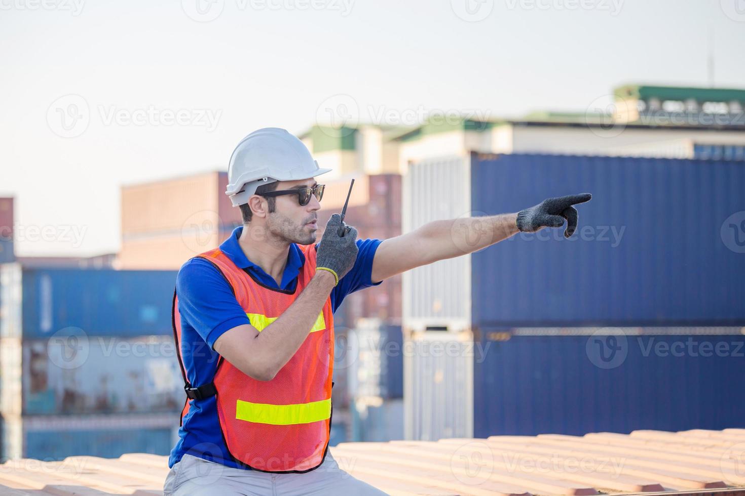 Foreman in hardhat and safety vest talks on two-way radio control loading containers box from cargo photo