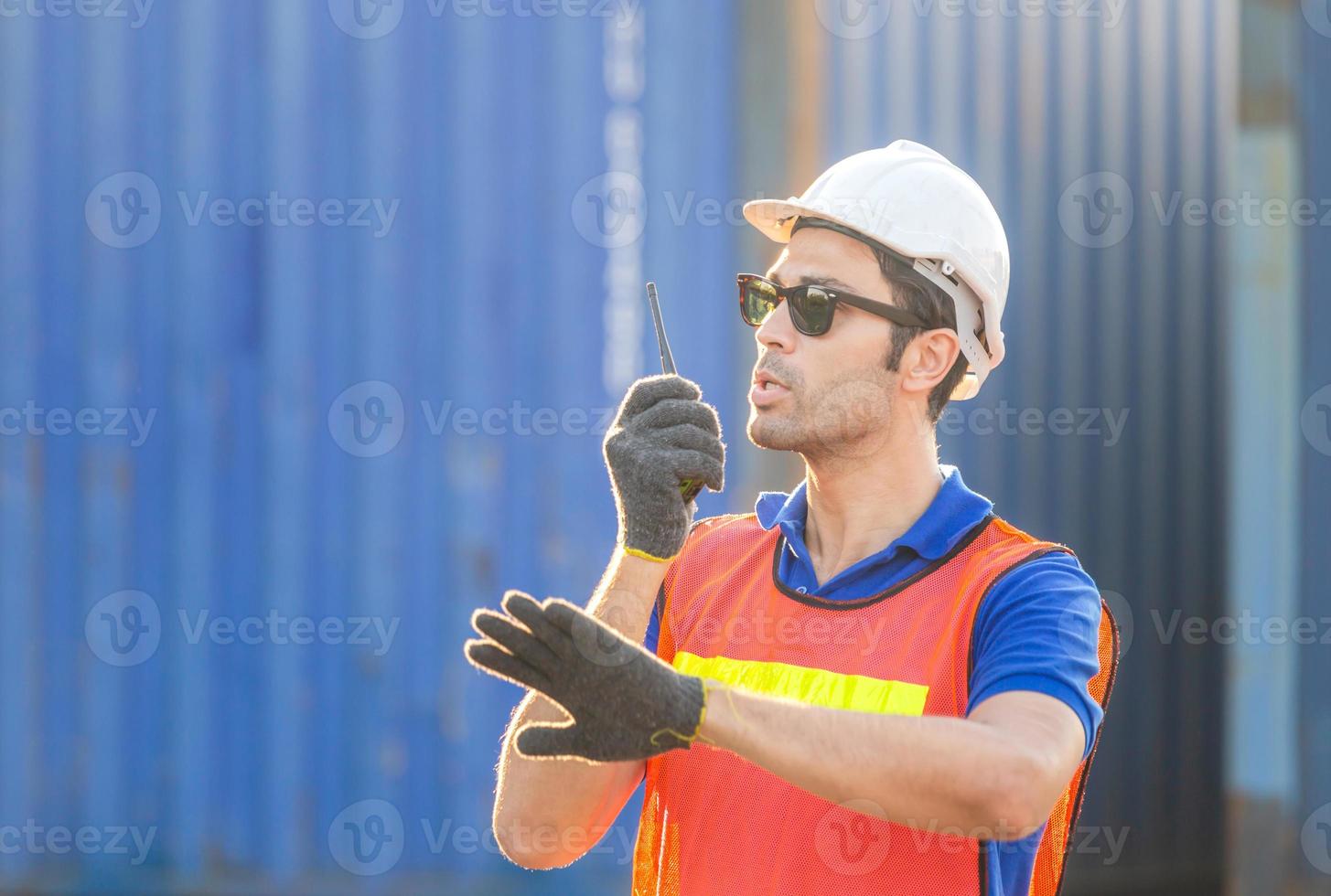 Foreman in hardhat and safety vest talks on two-way radio control loading containers box from cargo photo