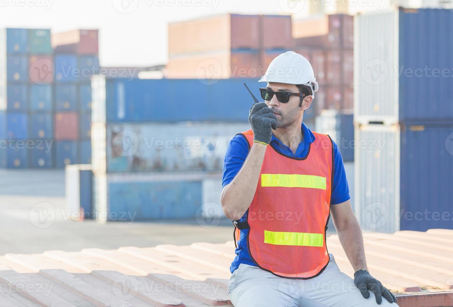 Foreman in hardhat and safety vest talks on two-way radio, Factory worker control loading containers box from cargo photo
