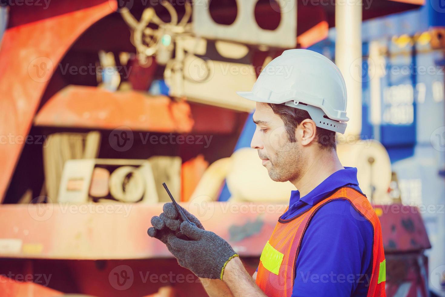 Foreman in hardhat and safety vest talks on two-way radio control loading containers box from cargo photo
