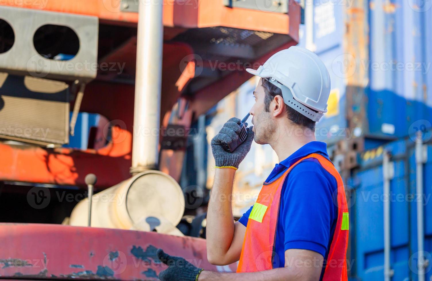 Foreman worker in hard hat and safety vest talks on two-way radio control loading containers box from cargo photo