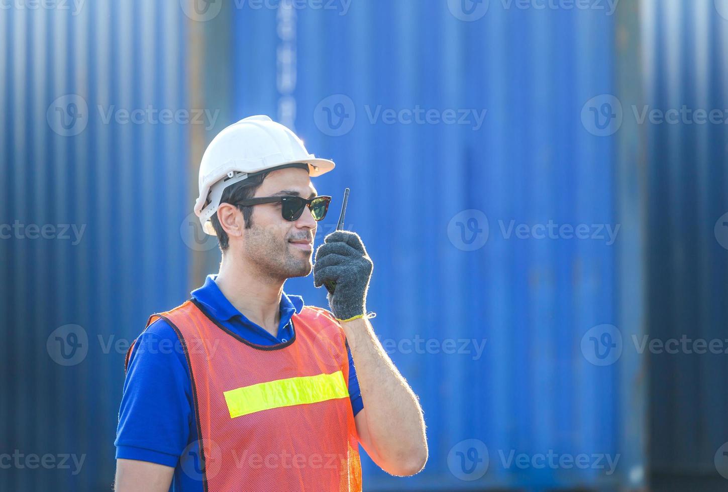 Happy foreman in hardhat and safety vest talks on two-way radio control loading containers box from cargo photo