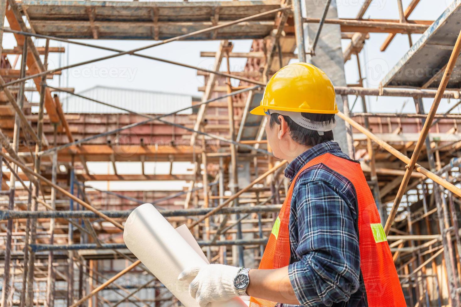 hombre trabajador con sombrero duro que sostiene el proyecto de planificación y verificación de planos en el sitio de construcción foto