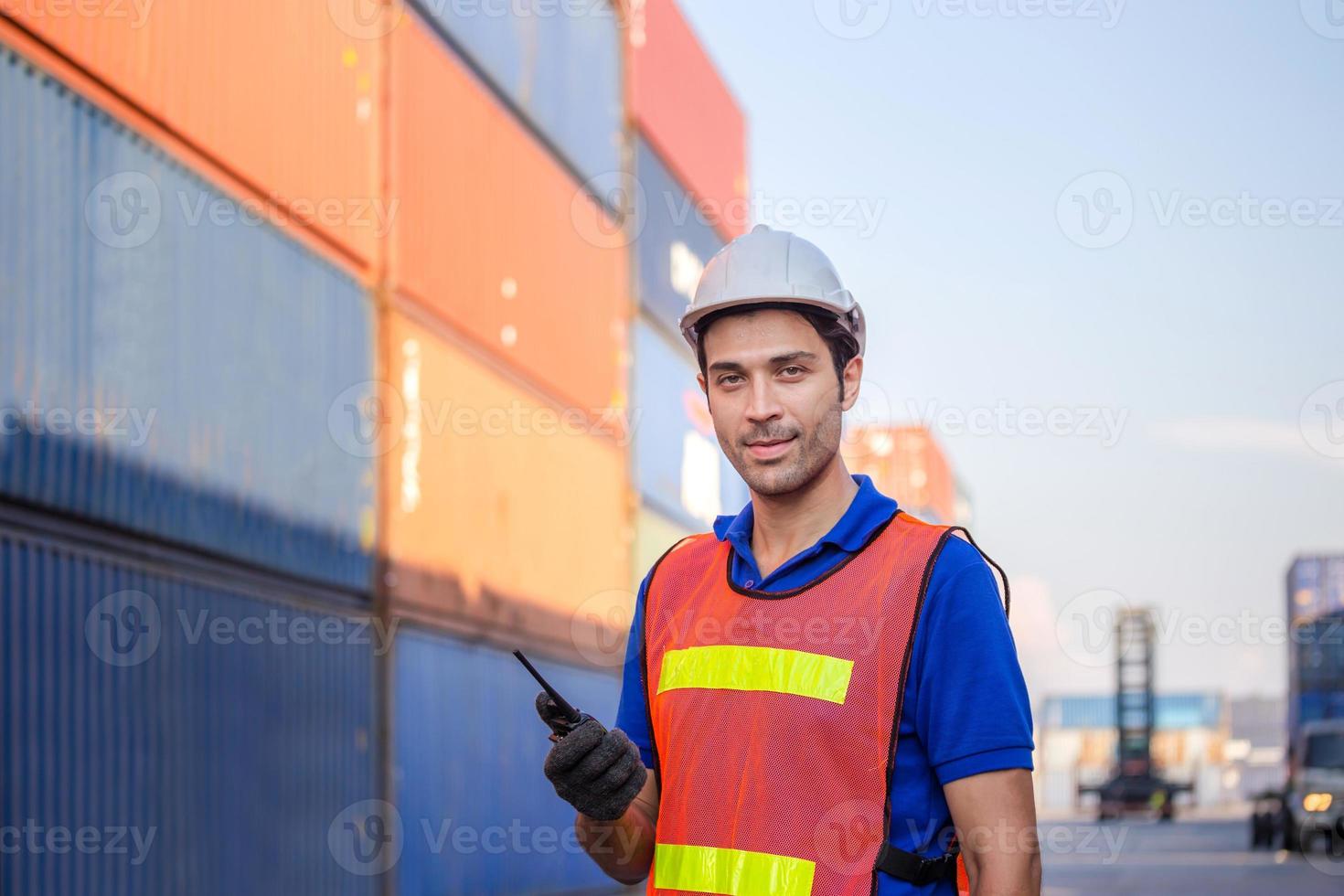 Smiling foreman in hardhat and safety vest talks on two-way radio control loading containers box from cargo photo