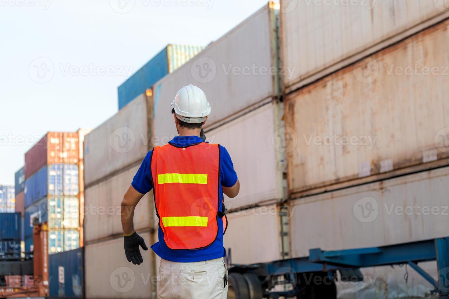 Foreman in hardhat and safety vest talks on two-way radio control loading containers box from cargo photo