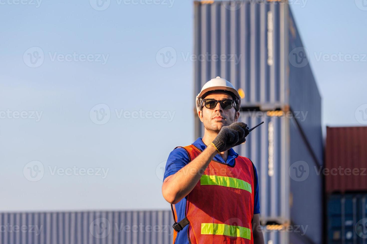 Foreman in hardhat and safety vest talks on two-way radio control loading containers box from cargo photo