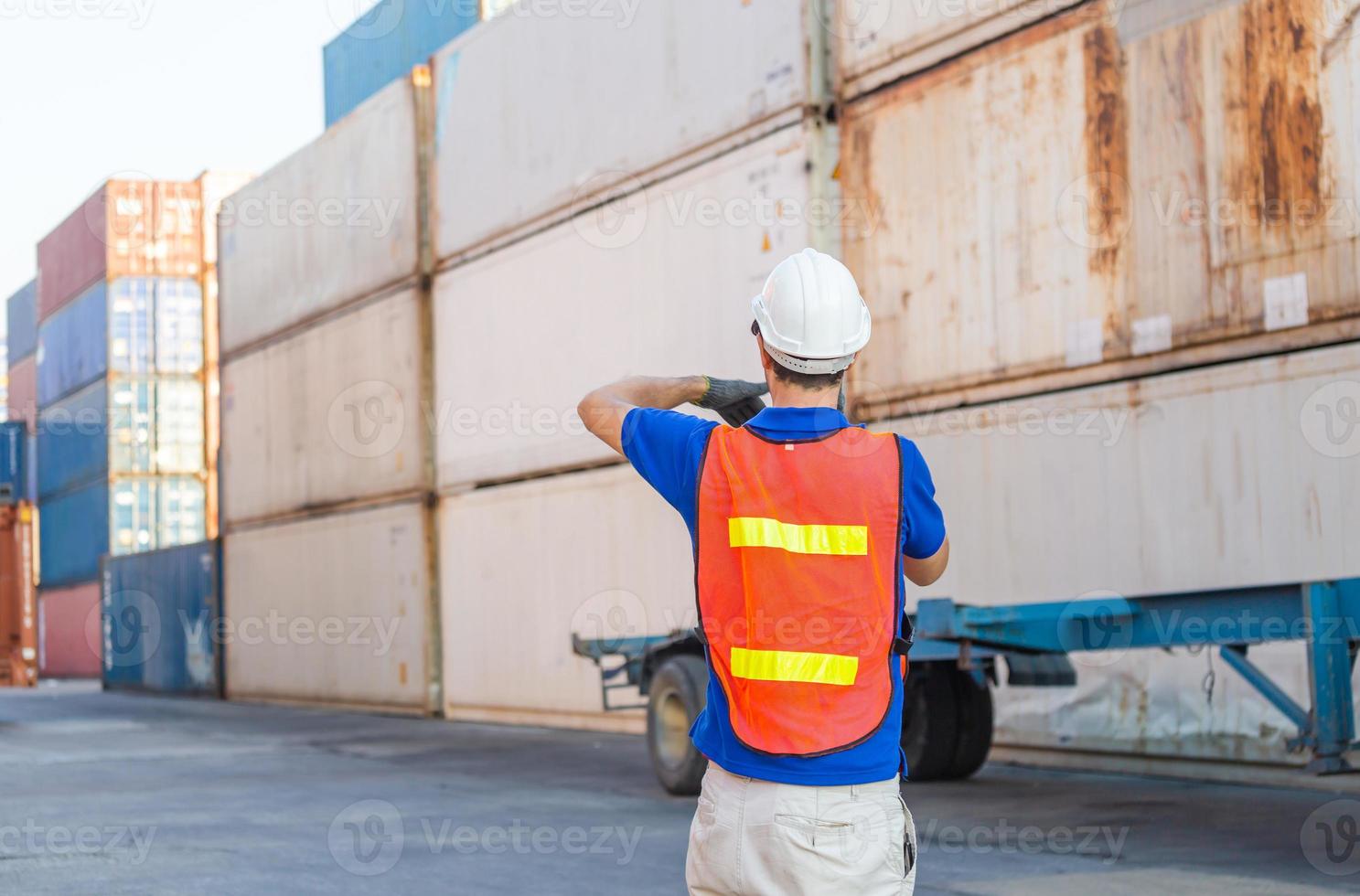 Foreman worker in hard hat and safety vest talks on two-way radio control loading containers box from cargo photo