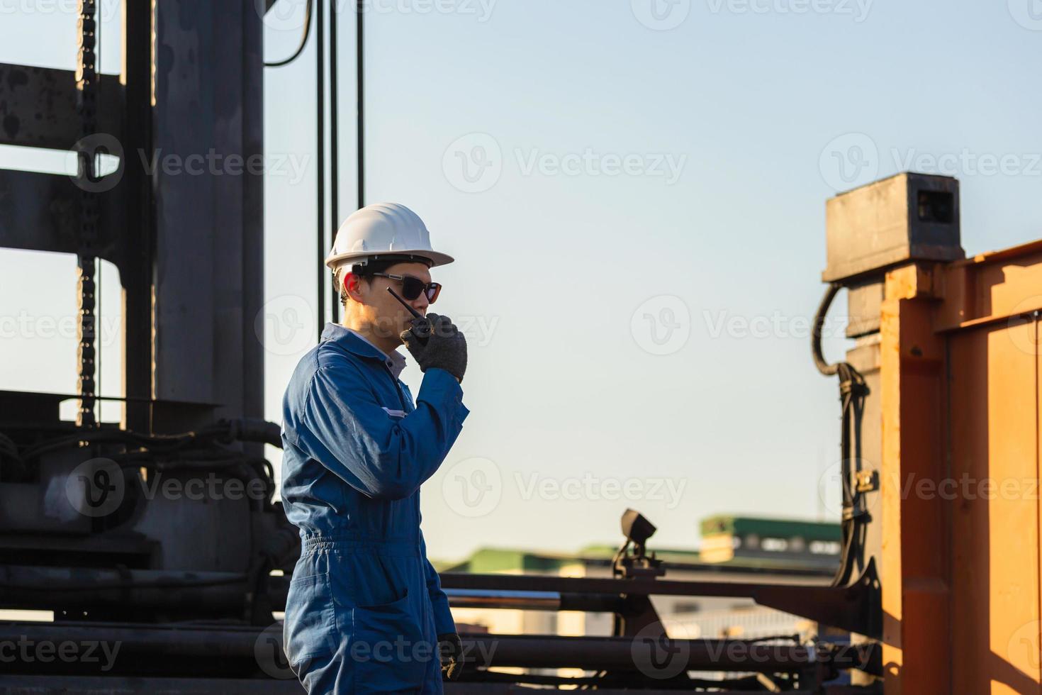 Foreman worker in hardhat and safety vest talking on two-way radio control loading containers box from cargo photo