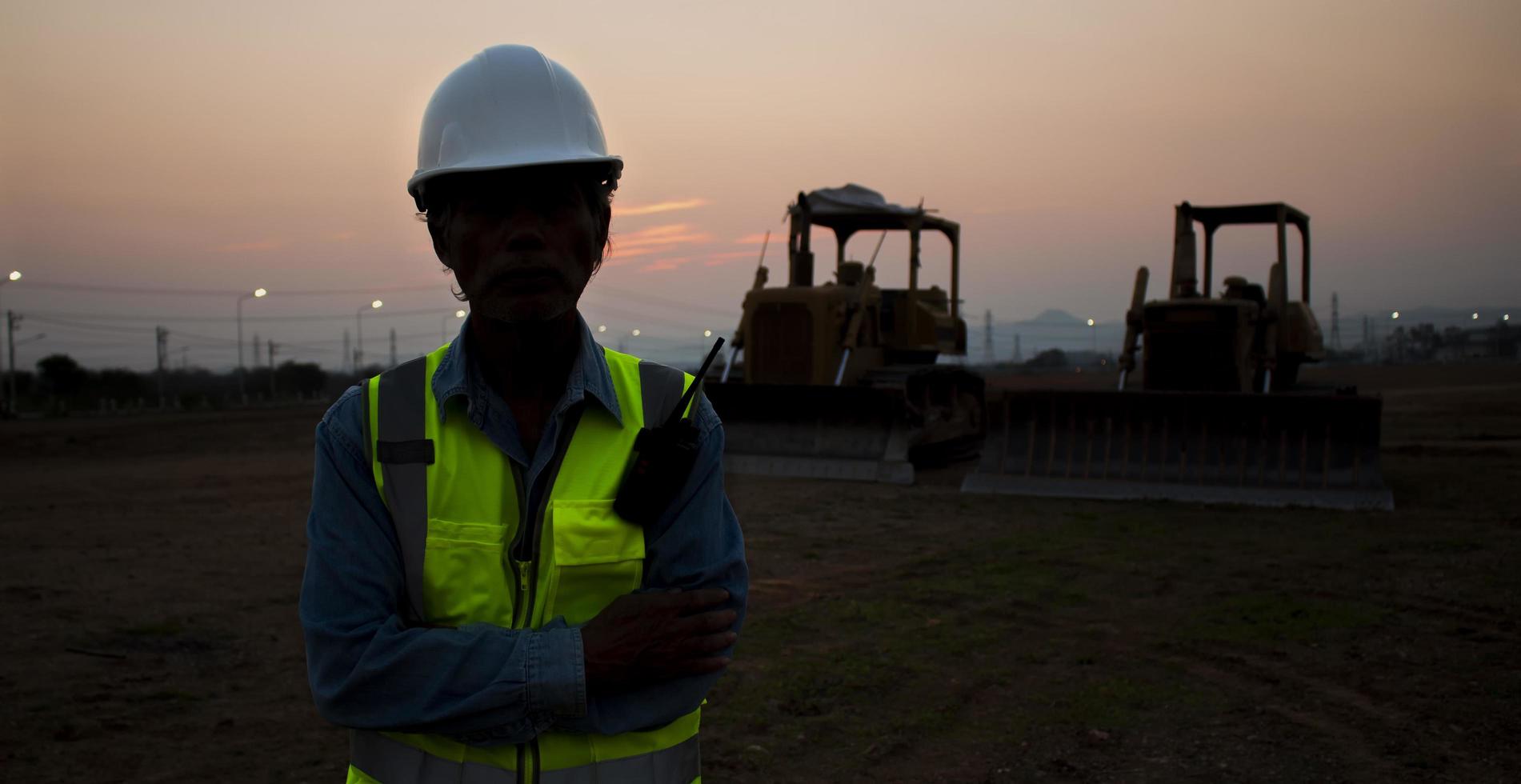Silhouette senior engineer wearing helmet and reflective vest on sunset background and crawler bulldozer. photo