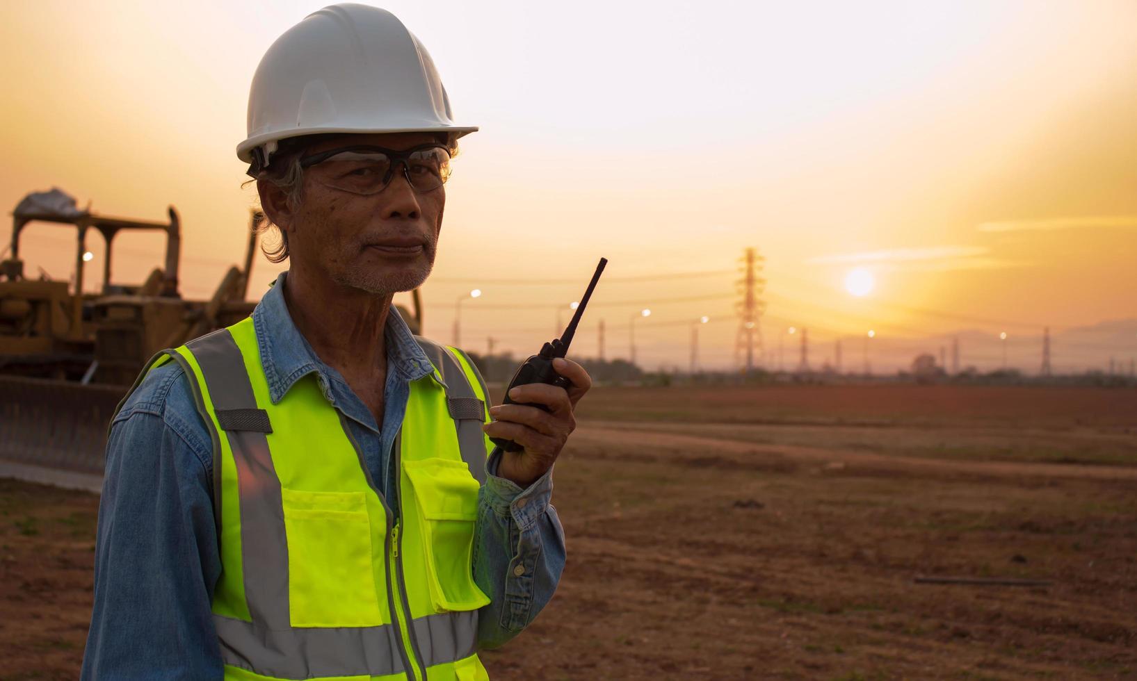 Silhouette Senior Engineer Wear a helmet and a reflective vest on a sunset background and a crawler bulldozer. photo