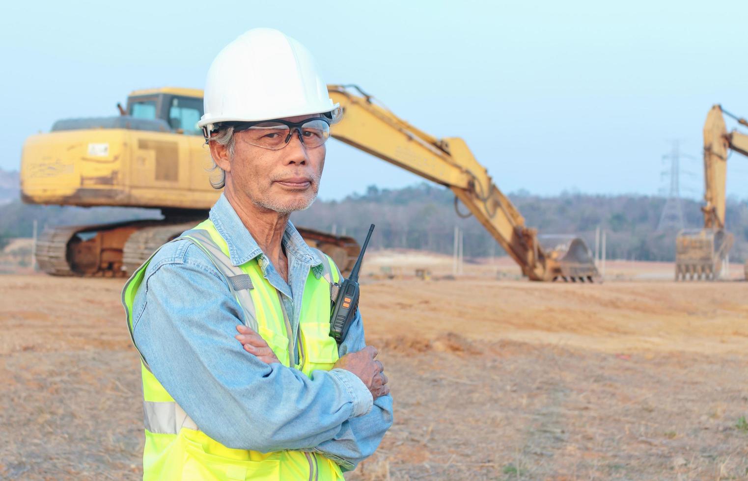 Portrait of an Asian male senior engineer wearing a vest and helmet inspects civil works, a middle-aged foreman controls an excavator. photo