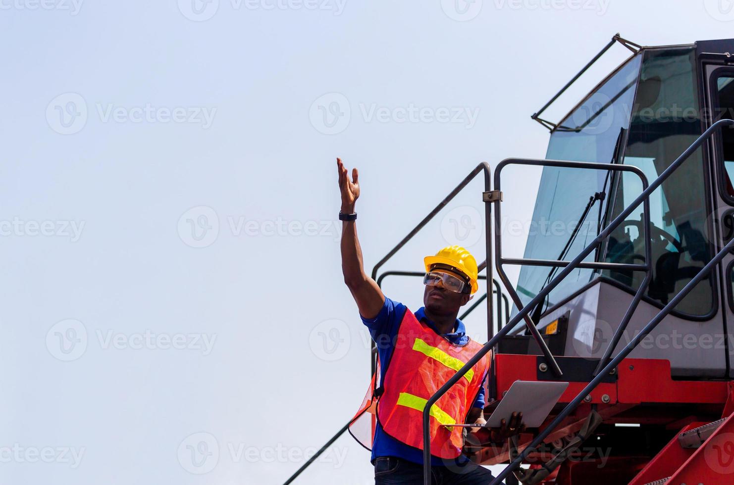 Worker man in hardhat and safety vest holding laptop standing on container stackers control loading containers box from cargo photo