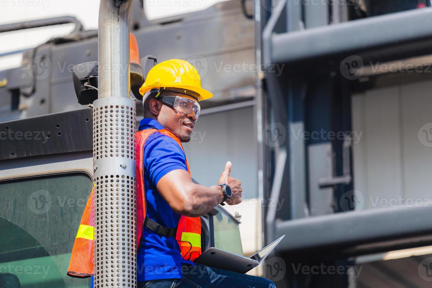 Worker in hardhat and safety vest holding laptop standing on container stackers control loading containers box from cargo, Smiling man and giving thumbs up photo