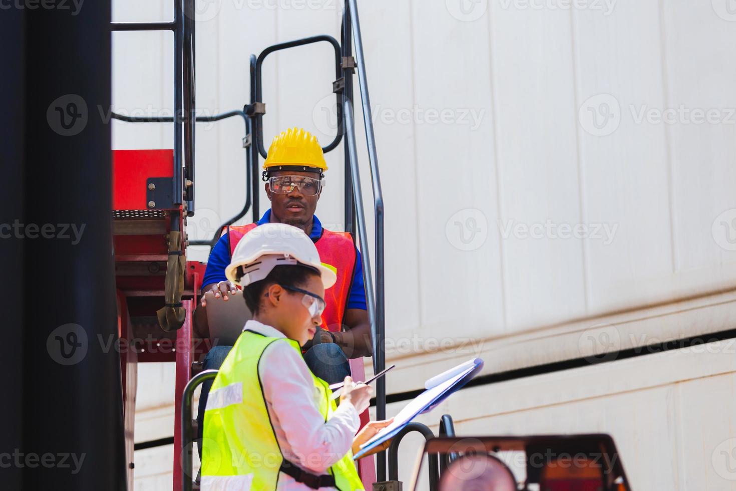 Female foreman safety vest using clipboard checklist and Worker man in hardhat holding laptop for control loading containers box from cargo photo