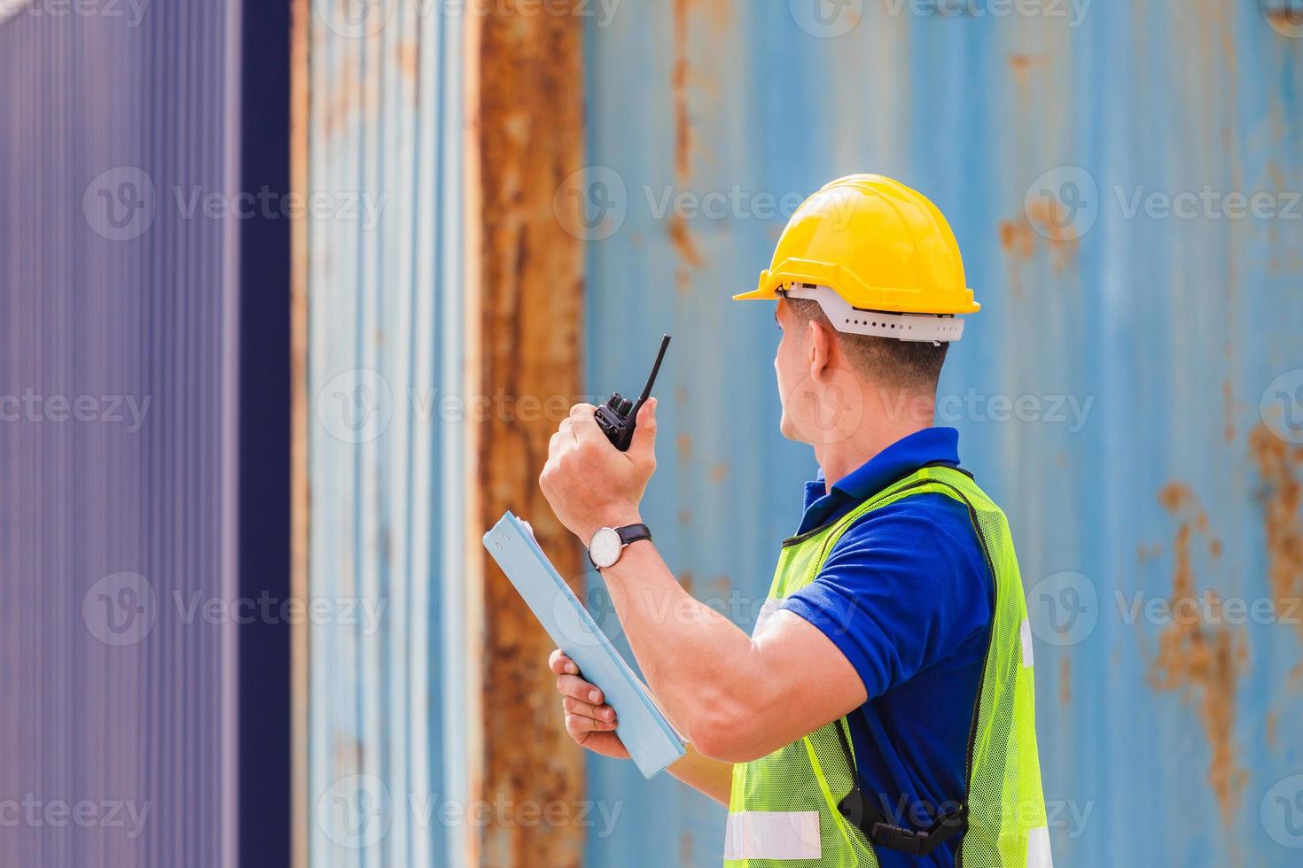 Foreman in hardhat and safety vest talks on two-way radio control loading containers box from cargo photo