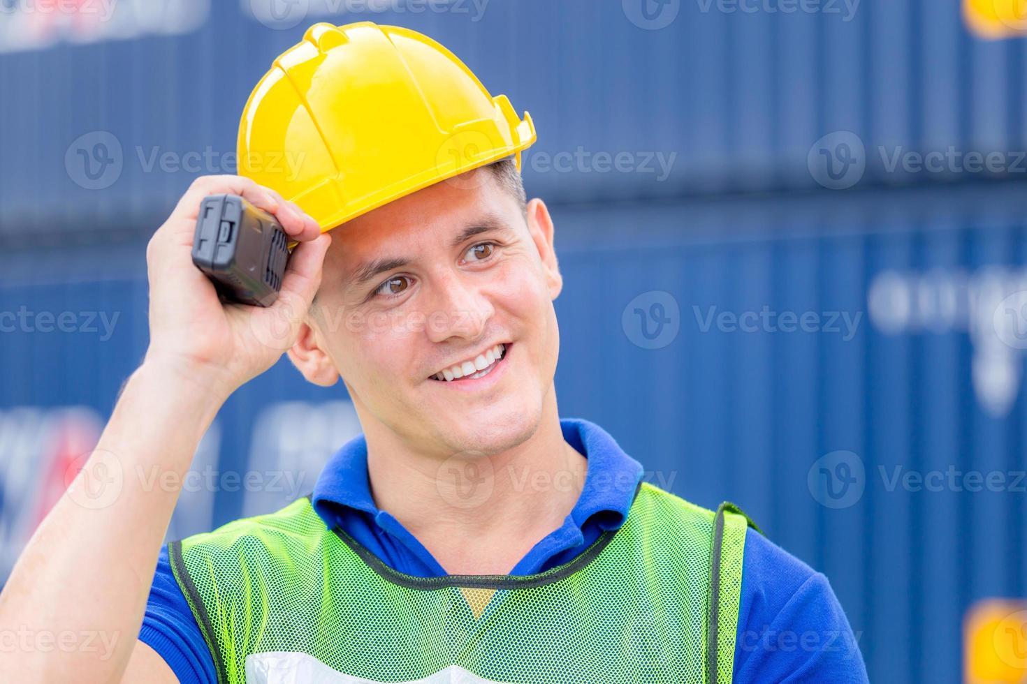 Happiness foreman in hardhat and safety vest talks on two-way radio control loading containers box from cargo photo