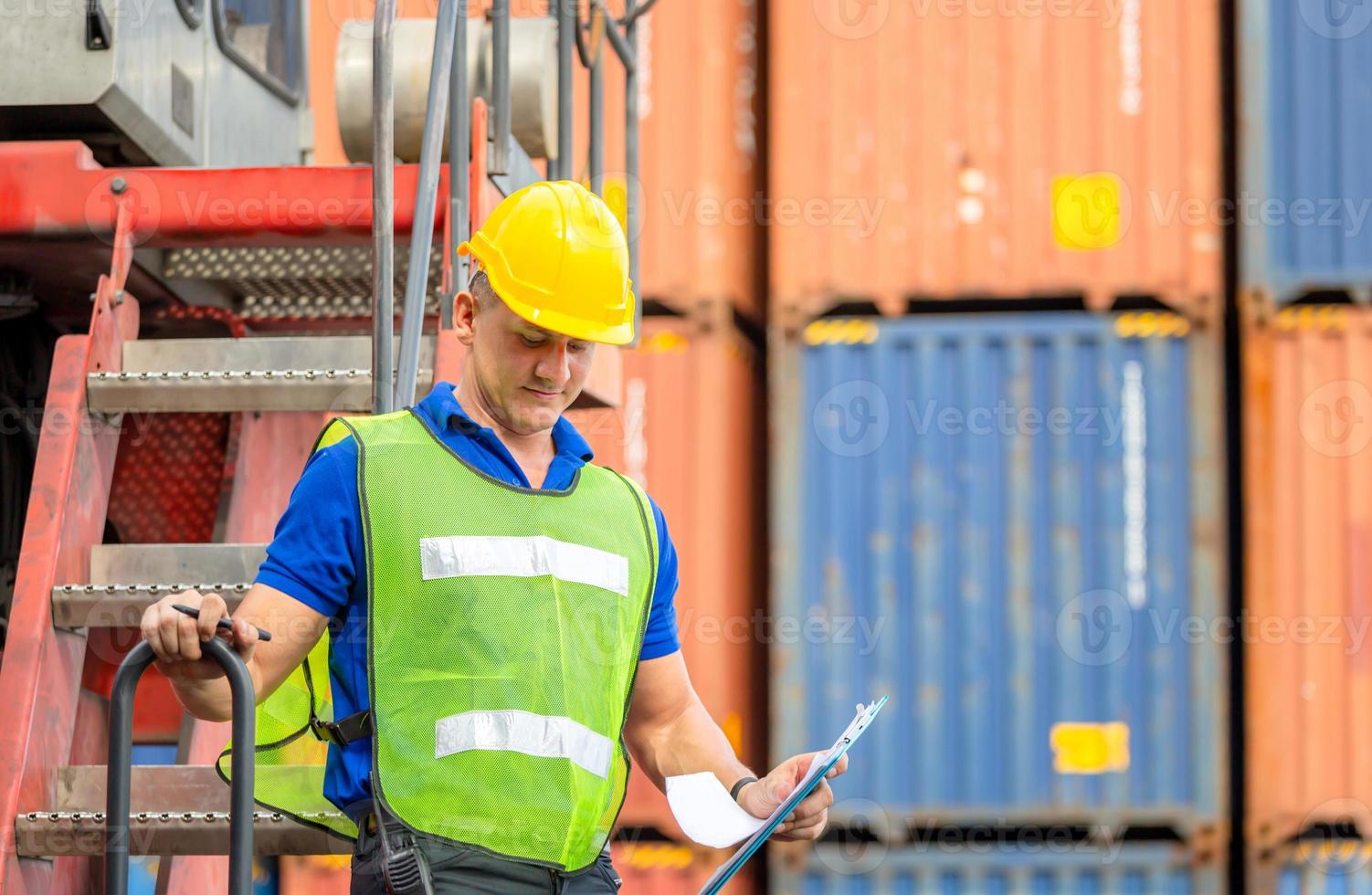 Worker man in hardhat and safety vest standing on container stackers control loading containers box from cargo photo