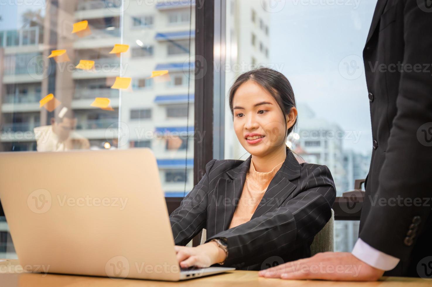 mujer de negocios escribiendo en la computadora portátil. jefe parado cerca del empleado y controlando el proceso foto