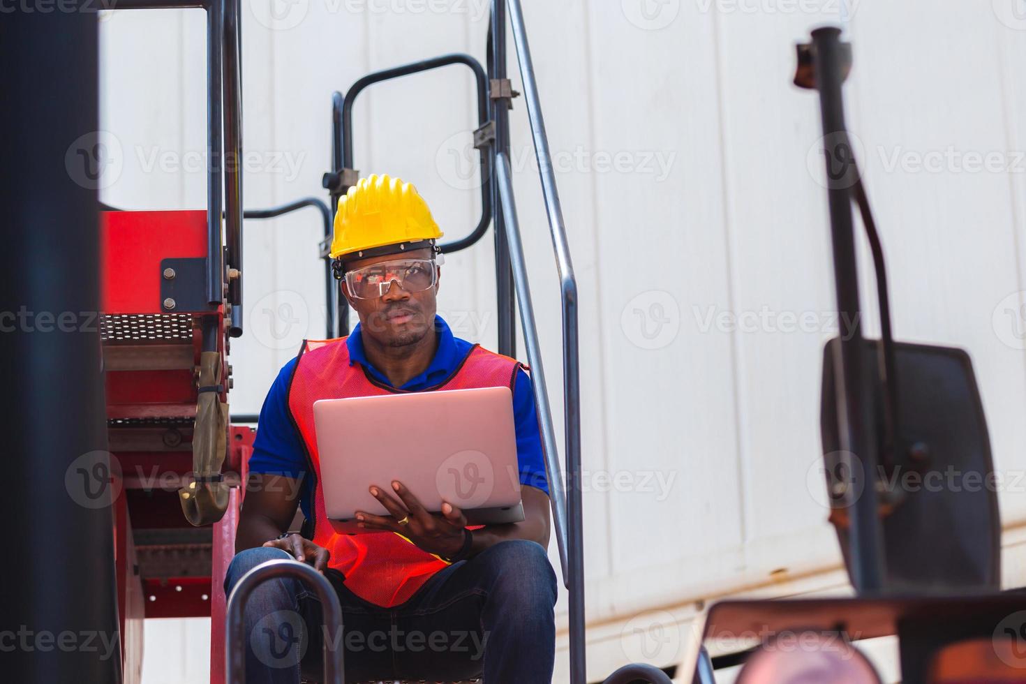 Worker man in hardhat and safety vest holding laptop standing on container stackers control loading containers box from cargo photo