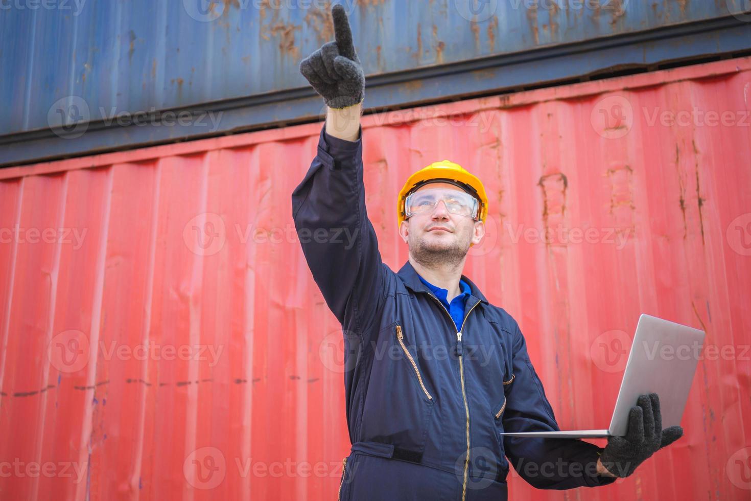 Worker man in hardhat and safety vest holding laptop and point to the sky, Foreman control loading containers box from cargo photo
