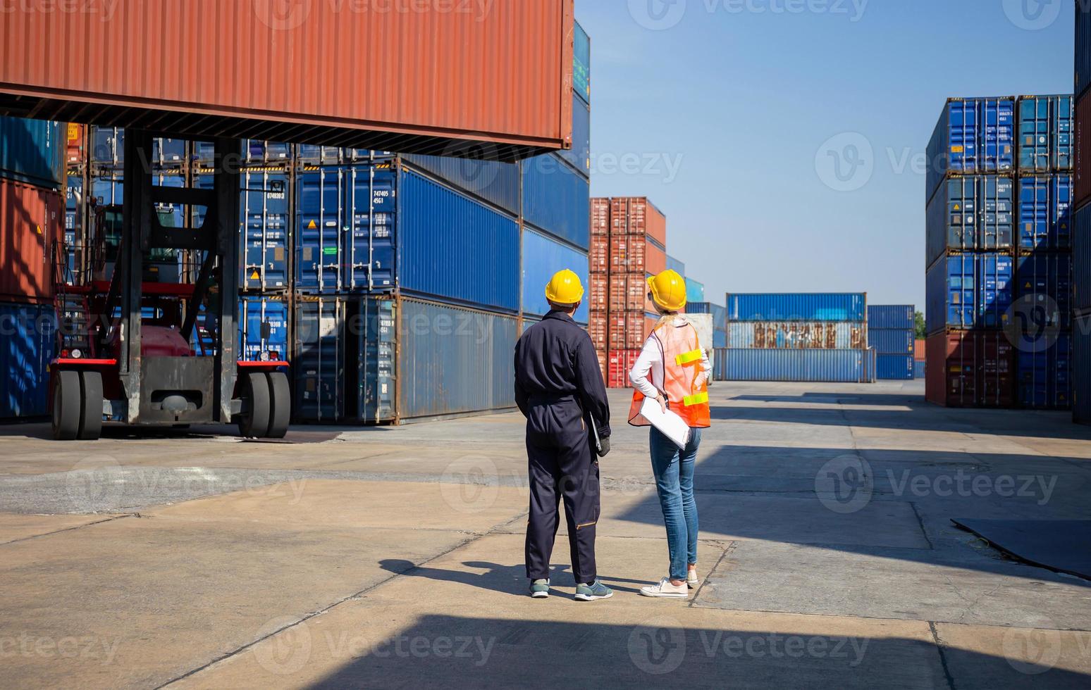 Worker man in hardhat holding laptop and Female foreman with safety vest checking and control loading containers box from cargo photo